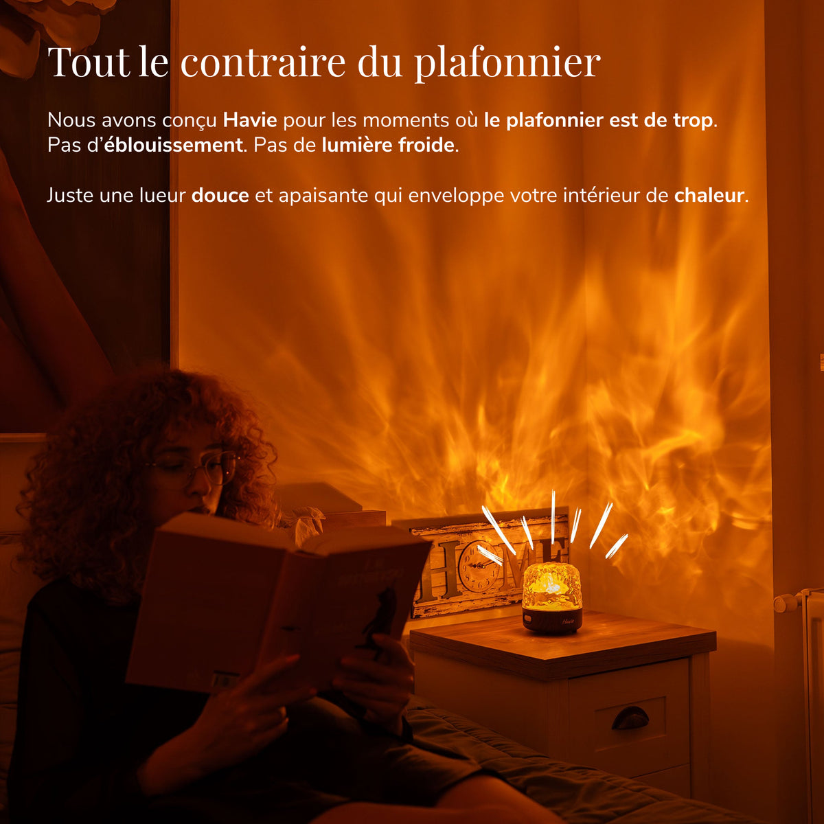 Une femme lit à côté de Havie, qui baigne une chambre douillette d'une lueur orange chaleureuse.