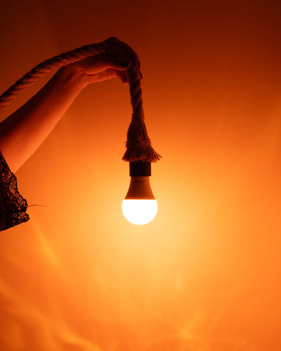 Des mains tiennent une lampe allumée suspendue à une cordelette
