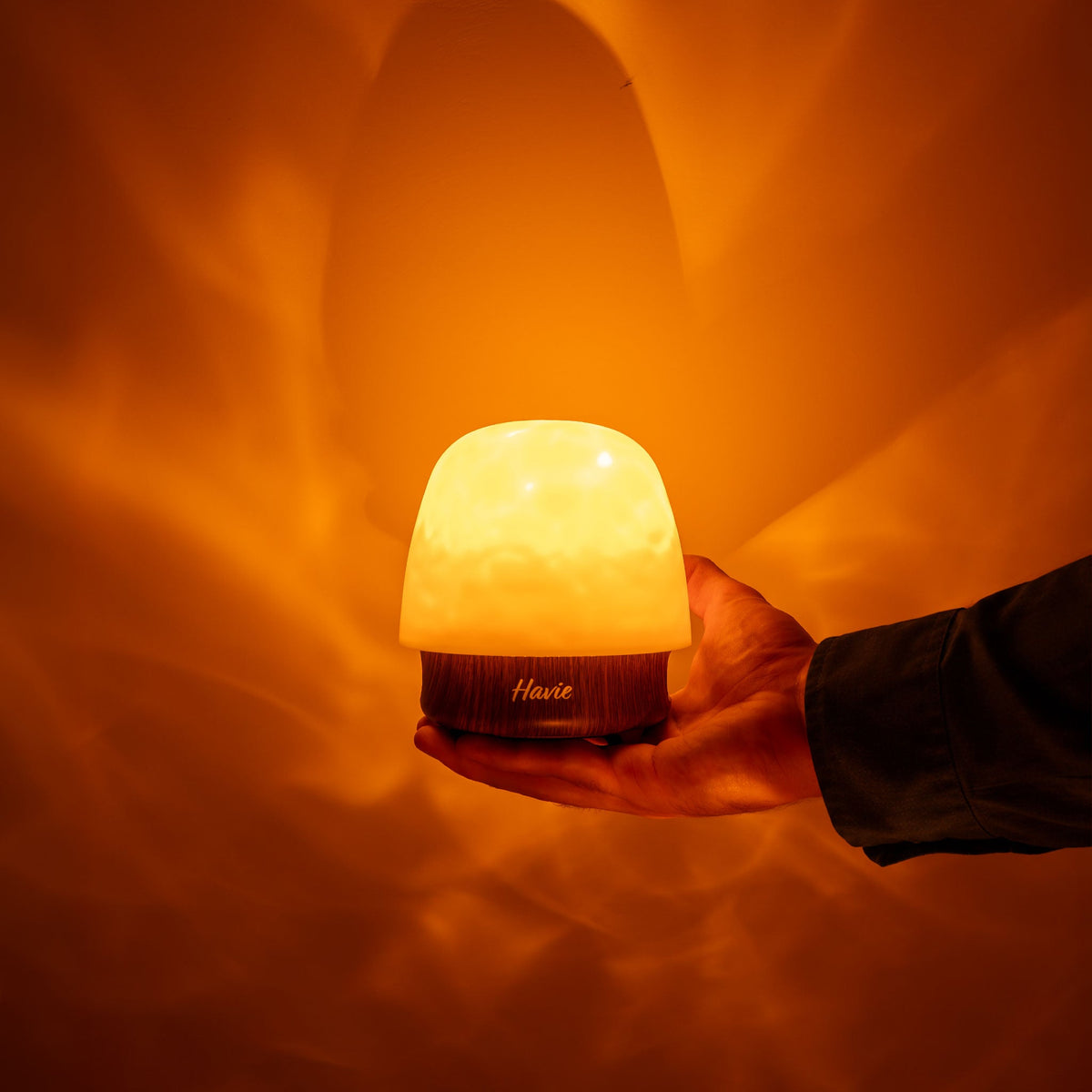 La veilleuse rechargeable Havie, tenue dans une main, diffuse une lueur orange chaleureuse.