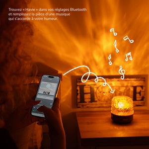 Une personne connecte son téléphone à Havie en Bluetooth pendant que la lampe remplit la pièce d'une lumière chaude.