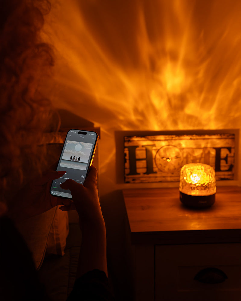 Une main choisit un son sur le téléphone pendant que Havie brille sur la table de chevet et que des reflets de flammes envahissent le mur
